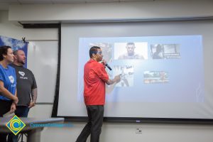 Man in a red shirt pointing to a projection screen.