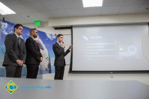 Three men in suits pointing to a projection screen,