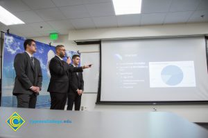 Three men in suits pointing to a projection screen,