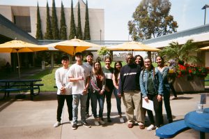 Group of students pose for photo in front of tables. Photo taken for Disposable Camera Project.