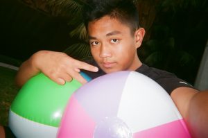 Student poses for selfie with multiple beach balls. Photo taken for Disposable Camera Project.