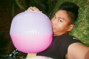 Student poses for selfie with multiple beach balls. Photo taken for Disposable Camera Project.