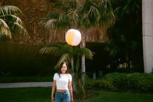 Student poses with floating beach ball above head. Photo taken for Disposable Camera Project.