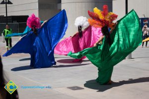 Performers wearing gold top and shorts with feathered headdress and colorful expanded fabric wings dancing at the 50th Anniversary Festival and Reunion.