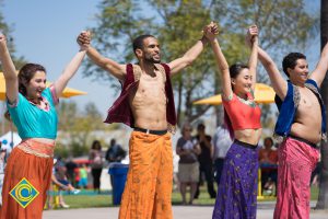 Young men and women in colorful costume holding hands with arms raised.