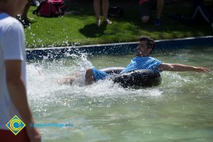 A young man in a blue and white old time bathing suit in the pond in an inner tube.