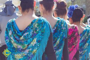 The backs if women with colorful floral scarves around their shoulders.