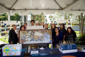 Dr. Therese Mosqueda-Ponce with her Puente students standing behind the framed Puente mural at the Puente booth.