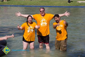 Three people in gold t shirts and shorts in the pond.