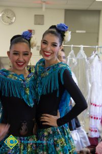 Two young girls smiling with hair pulled back with flowers in their hair and multi-colored costumes.