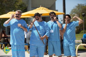 Four men with fake moustaches and blue and white stripped shirts and shorts.