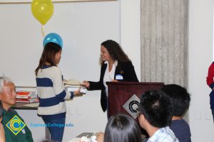 A student in a blue and white striped sweater receiving an award from a woman with long curly hair and a white shirt and black jacket.