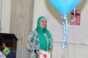 A woman smiling in a white, blue and teal shirt with a teal hajib.