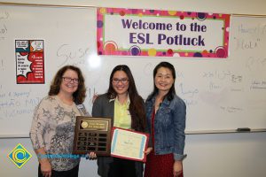 A student holding an award with two staff members smiling.