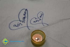 Two drawn hearts with writing in them and a lit candle next to them.
