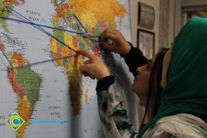 Two young ladies attaching string to push pins on a world map.