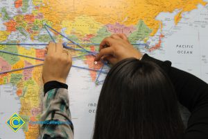 A hand attaching string to push pins on a world map.
