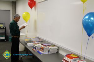 A man standing at a table of stacked books reading.