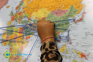 A hand attaching string to push pins on a world map.