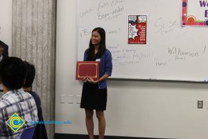 A young lady in a blue sweater and black dress holding a certificate.