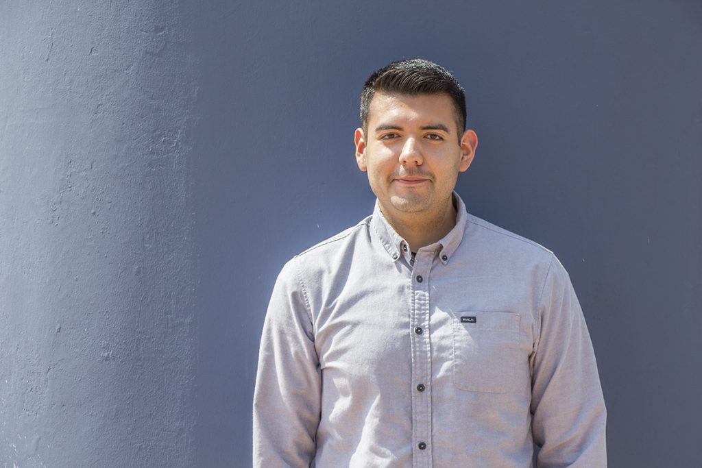 Man in gray button-down long-sleeved shirt smiles at camera