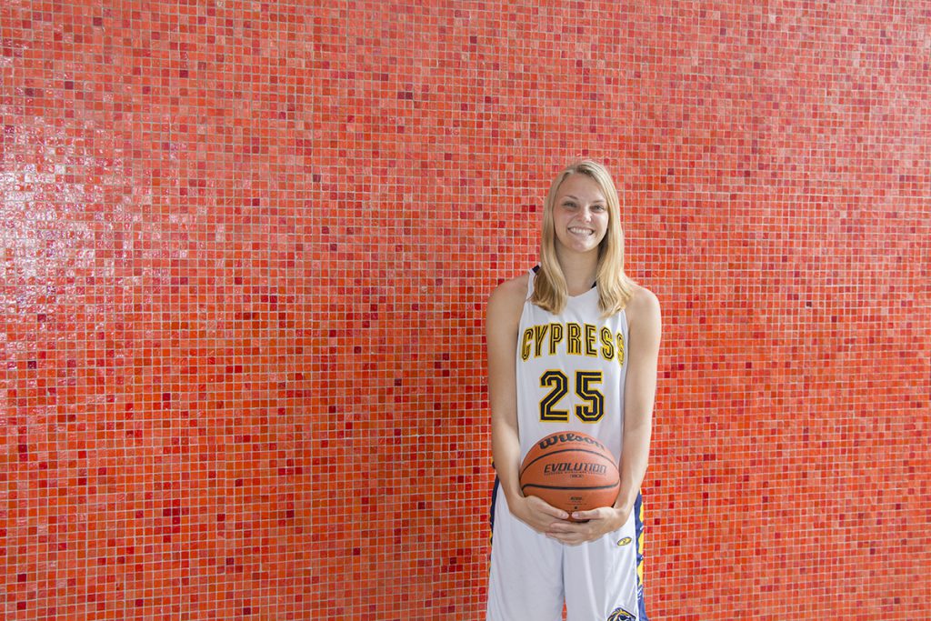 Blond woman in basketball uniform stands in front of orange tiled wall