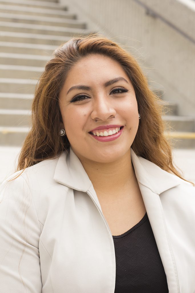 Hispanic woman smiles, wearing khaki blazer and black top