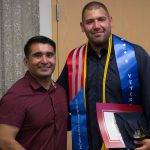 Veteran graduate wearing his regalia standing with Juan Garcia.