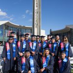 A group of Veteran graduates wearing graduation regalia with the campanile in the background.