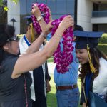 Two students having graduation leis of purple orchids placed over their heads.