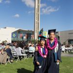 Female and male students in cap and gown wearing purple orchid leis.