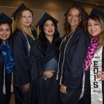 Five young ladies wearing graduation regalia smiling.