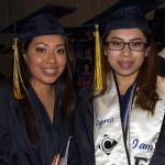 Two young ladies wearing graduation regalia smiling.
