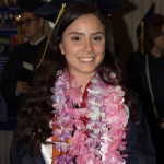 A young lady wearing graduation regalia and pink and purple leis.