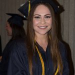 A smiling young lady with long brown hair in graduation regalia.