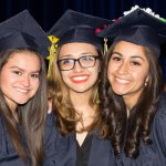 Three smiling young ladies in graduation regalia.