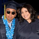 Young man in sunglasses and blue lei and young lady smiling in graduation regalia.