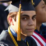 A young man looking at the camera in his cap and gown.