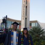 Two graduates standing in front of the campanile.