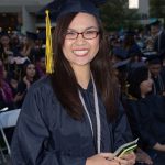 A smiling young woman with glasses in graduation regalia