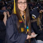 A smiling young woman with glasses in graduation regalia