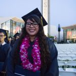 Smiling female graduate with glasses wearing a purple orchid lei.