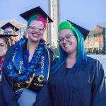 Two smiling female graduates with colorful hair.