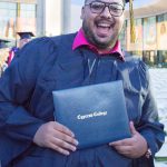 Young man in graduation regalia smiling and holding diploma.