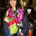 Smiling young lady in graduation regalia holding diploma and flowers.