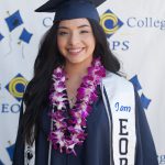 A female graduate wearing full regalia and EOPS stole and purple lei.