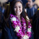 A young lady wearing graduation regalia and pink and purple leis.