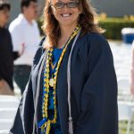 Young woman with brown hair and glasses wearing graduation gown and cords.