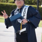 An EOPS graduate wearing gown and holding his cap and flashing the peace sign.