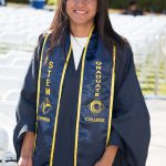 Young lady with long brown hair wearing graduation regalia with STEM stole and holding her cap.